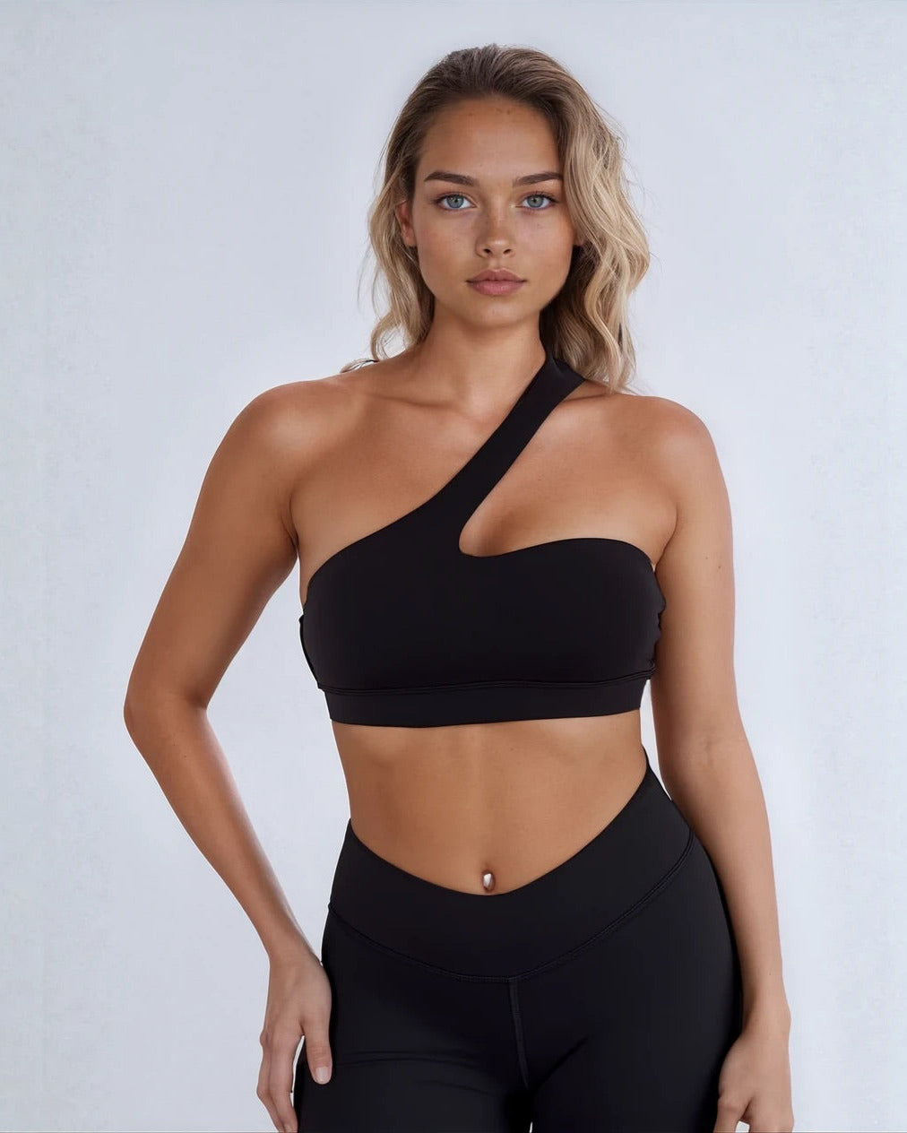 Woman wearing a black one-shoulder top and leggings on a white background