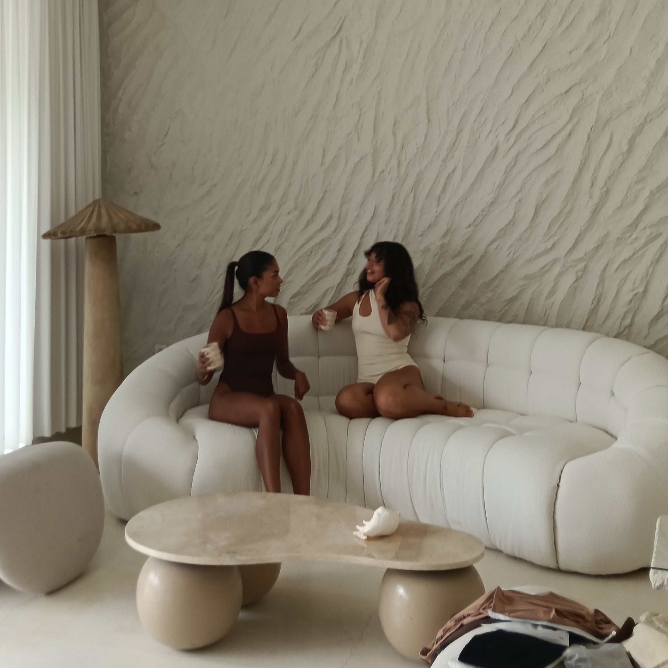 Two women sitting on a modern white sofa in a stylish room with a textured wall.