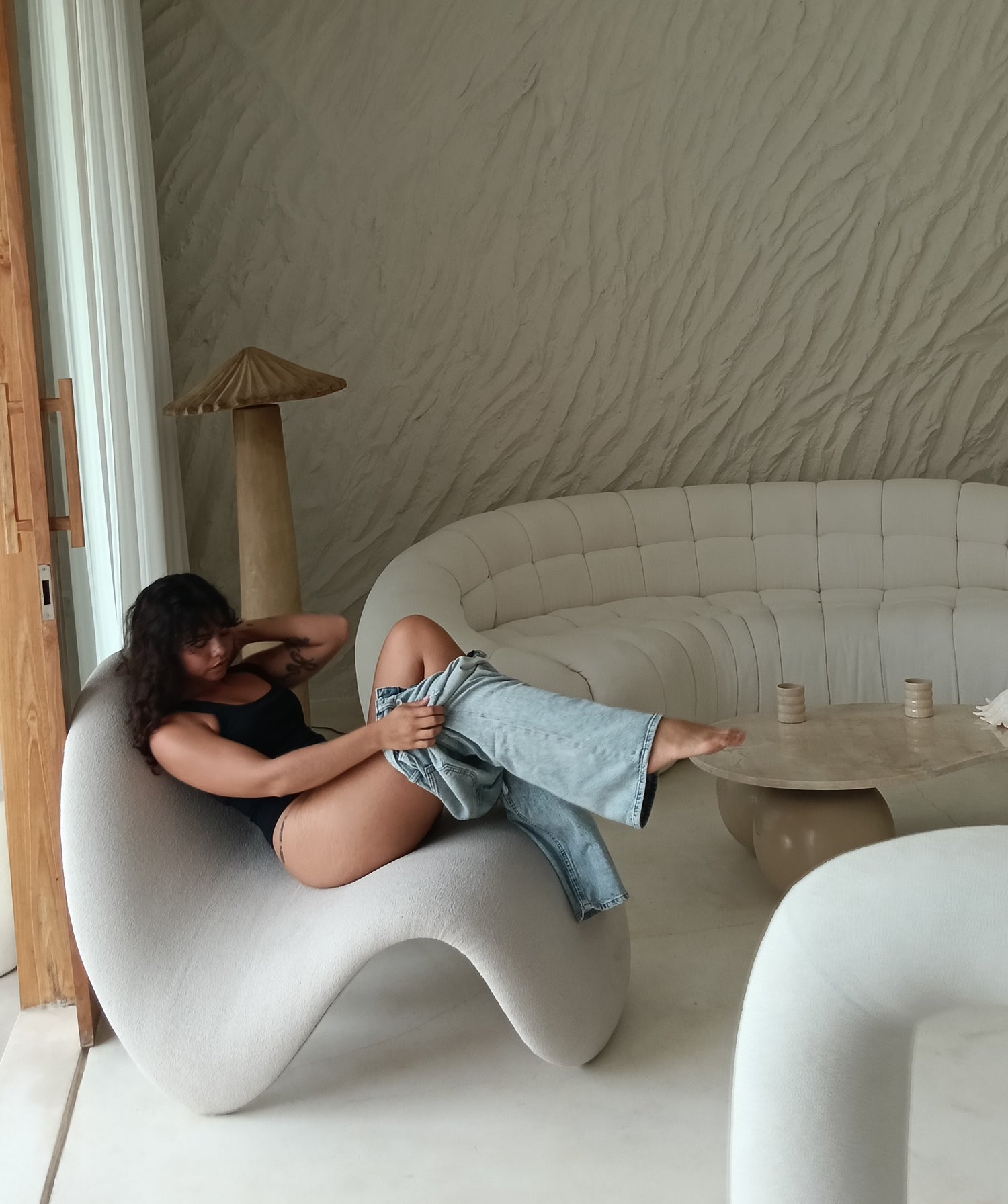 Woman sitting on a modern white chair in a stylish room with a textured wall.